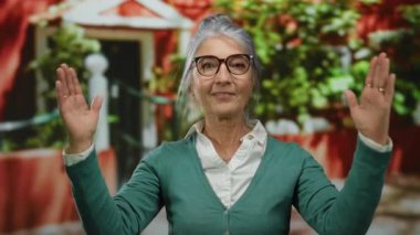 Canlı bir sokak arkaplanında el hareketleriyle gri saçlı yaşlı bir kadın şehir ortamında kendine güven ve dışavurumculuk gösteriyor..