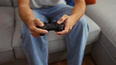 Evdeki kanepede oturmuş video oyunu oynayan genç bir adam, iki eli de rahat bir şekilde oyun kumandasını tutuyor..