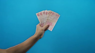 İzole edilmiş mavi arka planda Türk lirası banknotları tutan adam, finans ve döviz kurları kavramını vurguluyor.
