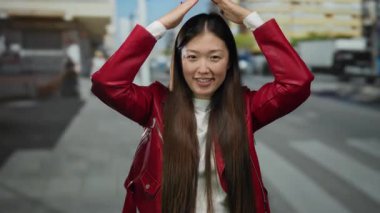 Kırmızı ceketli bir kadın, bir şehir caddesinde neşeli bir şekilde gülümsüyor ve poz veriyor, şehir modasını ve canlı bir açık hava havasını sergiliyor..