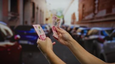 Kentsel bir sokakta Meksika pezosu tutan adam, hareketli bir şehir ortamında para alışverişini ve mali bağlamı vurguluyor..