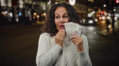 Tayvan banknotlarını elinde tutan orta yaşlı bir kadın. Canlı bir şehir caddesinde, şaşırdığını, rahat bir kazak giydiğini, finansal kazancı ya da alışverişi sembolize ettiğini söylüyor..