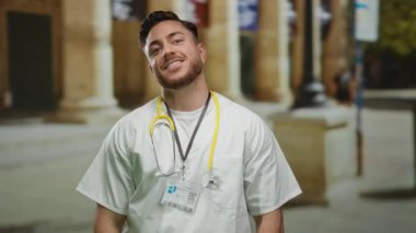Steteskoplu genç bir erkek doktor, şehir caddesinde canlı bir açık havada gülümsüyor ve profesyonel sağlık hizmetlerini sergiliyor..