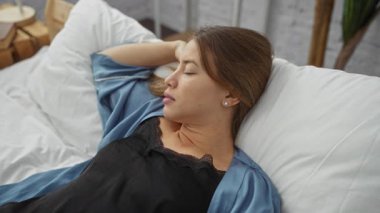 Rahat bir yatak odasında huzur içinde uyuyan bir kadın, yumuşak yastıklarla çevrili, beyaz bir yatakta uzanıyor, ve evin içinde sakin bir ortam, bir rahatlama ve sükunet anı yakalıyor..