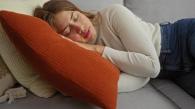 Evdeki rahat bir kanepede huzur içinde uyuyan, rahat bir turuncu yastığın üzerinde dinlenen, huzurlu ve rahatlatıcı bir atmosfer yaratan bir kadın..