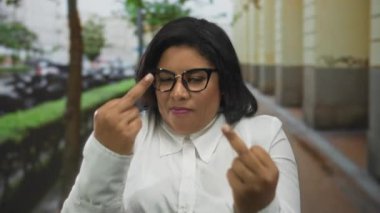 Gözlüklü, kendinden emin, iri yarı, İspanyol bir kadın, şehir geçmişinin bulanık olduğu kalabalık bir caddede cesur bir hareketle tavır sergiliyor..