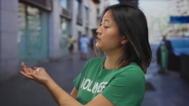 Yeşil tişörtlü genç bir kadın şehir sokağında elini uzatıyor. Nezaket ve toplum ruhunu gösteriyor..