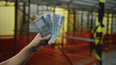 Dışarıdaki inşaat sahasında Macar banknotları tutan bir adam endüstriyel geçmişi ve güvenlik engelleri olan finansal iş kavramını gözler önüne seriyor..