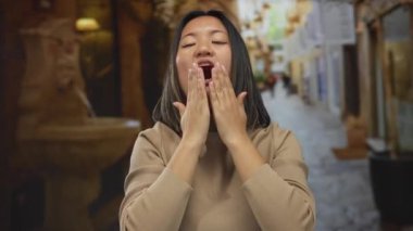 Kalabalık bir sokak arkaplanında sevinçle gülümseyen genç bir kadın sıcak şehir atmosferiyle çevrili göğsüne sarılmış ellerle minnettarlığını ifade ediyor..