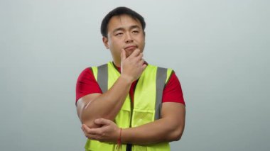 Beyaz arka plan üzerine güvenlik yeleği giyen adam düşünceli ve düşünceli görünüyor. Yapı ve güvenlik fikirlerini somutlaştırırken rahat ve rahat bir duruş sergiliyor..