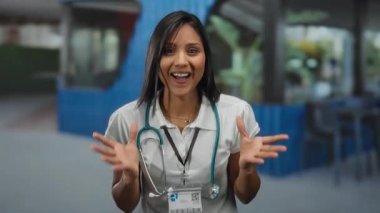 Sokak terasında steteskopla gülümseyen İspanyol kadın doktor sağlık ve kentsel çevre karışımını öneriyor..