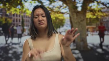 İnsanlar ve ağaçlarla çevrili güneşli bir şehirde, açık havadan hoşlanmadığını ifade eden bir kadın, şehir yaşamında samimi bir anı yakalıyor..