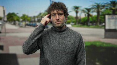 Genç İspanyol bir adam, şehir caddesinde özgüvenli ve çekici bir tavır sergileyerek düşünceli bir şekilde kameraya doğru işaret ediyor..
