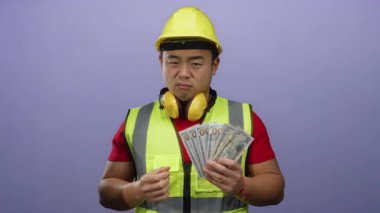 Miğfer takan genç bir adam mor bir arka plana karşı düşünceli bir ifadeyle bize dolar tutuyor..