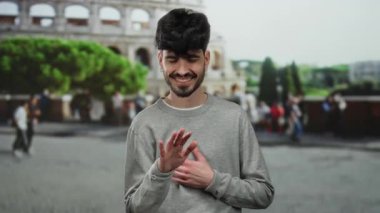 Roma ikonik kolezyumunun önünde gülümseyen genç bir adam, canlı bir sokak atmosferiyle şehir merkezinde sıradan bir açık hava anını yakalıyor..