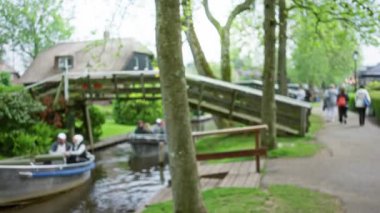 Kanalda tekneli giethoorn 'un bulanık görüntüsü ve Hollanda' da yemyeşil yemyeşil bir köprü etrafında yürüyen insanlar..