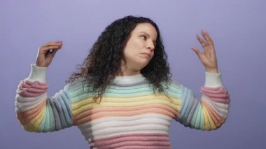 Renkli süveter giymiş bir kadın, izole edilmiş mor duvara karşı jest yapıyor, etkileyici ve düşünceli titreşimler yayıyor İspanyol kimliğini ve duygusunu belirgin bir şekilde yakalıyor..