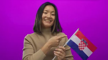 Ulusal gurur ve neşe dolu ifadeyi vurgulayan canlı pembe arkaplanlı gülen kadın Hırvat bayrağını işaret ediyor.