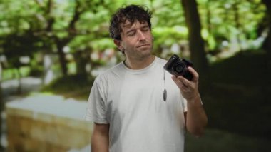 Yeşil park ortamında kamerayı tutan yakışıklı bir adam güneşli bir günde doğa ve sükunete odaklanmış fotoğrafçılık anları yakalıyor.