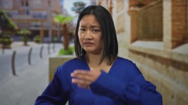 Genç Çinli kadın elleriyle gözlerini kapatıyor. Şehrin sokaklarında korku saçıyor. Mavi bir bluz giyiyor ve gündüz vakti dışarıda dikiliyor..