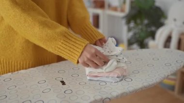 Çamaşır odasındaki ütü masasında giysileri katlayan, ev temizliği yapan, elleri ve kıyafetleri rahat ev ortamında odaklanan bir kadın..