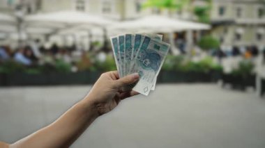 Şehir sokağının arka planında yerel ekonomiyi resmeden işlek bir restoran terasında elinde paralar tutan bir adam..