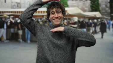 Gülümseyen adam hareketli bir şehir caddesinde fotoğraf jesti yapıyor, dinamik açık hava sahnesiyle meşgul oluyor..