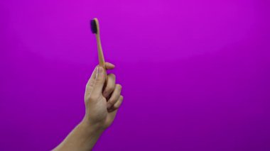 Erkek el bambu bir diş fırçasıyla izole edilmiş, pembe bir arkaplan üzerinde duruyor. Minimalist bir ortamda çevre dostu diş bakımı ürünlerini vurguluyor..