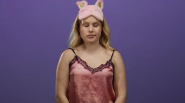 Pembe gecelikli bir kadın mor bir arka planda uykusuzluk jestleri yapıyor. Uyanık ve tetikte olduğunu gösteriyor..