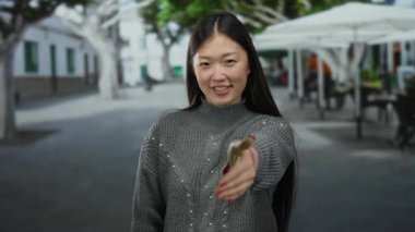 Şehir terası kafe sokağında elini sıkan kadın gri kazağıyla gülümsüyor.