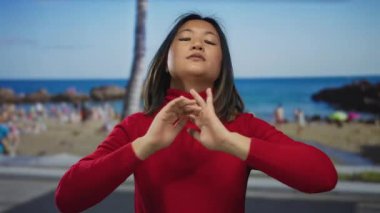 Sahilde kıyı kesiminde huzur ve sükunet içinde kırmızı bir süveter giyen, bulanık bir deniz kenarı arka planına sahip bir kadın..