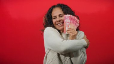 Kadın Filipinli pezo banknotlarıyla kırmızı arka planda kutluyor. Parayı kucaklıyor ve kameraya elini uzatıyor..