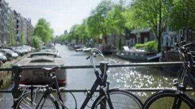Bulanık bisikletler, Amsterdam 'ın ağaçlarla ve bahar güneşinde büyüleyici binalarla kaplı manzaralı kanalına bakan bir köprüye yaslanıyor..