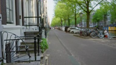 Geleneksel mimarisi, bisikleti ve yeşil bir gölgelik altındaki bir kanalı olan Amsterdam caddesinin odaksız görüntüsü..