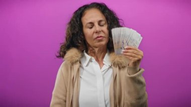 Elinde Singapur banknotları tutan orta yaşlı bir kadın, izole edilmiş mor duvar arkaplanına karşı taş jest yapıyor, zenginlik ve tutum taşıyor..