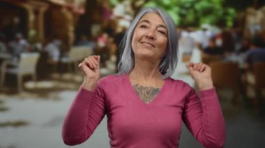 Gri saçlı yaşlı kadın, açık hava restoranının terasında para jesti yapıyor..