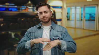 Sıradan kot ceketli sakallı genç adam spor salonunda arka planda bulanık spor ekipmanlarıyla fitness ortamını öneriyor.