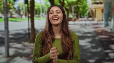 Canlı bir caddede mutlu bir şekilde gülümseyen bir kadın yeşil bir gömlek giyip, etrafı yemyeşil ağaçlarla çevrili..