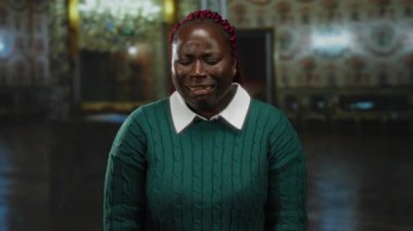 Yeşil kazaklı bir kadın müzede avize ve dekorasyonla iç mekanda ağlıyor. Kültür ortamında duygu ve iç gözlem uyandırıyor..