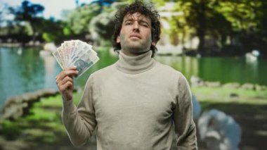 Parkta İspanyol bir adam elinde Polonya zloti banknotları ve kendinden emin bir ifadeyle..