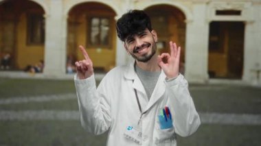 Laboratuvar önlüğü giyen İspanyol genç adam eski bir üniversite ortamında özgüvenle gülümsüyor akademik coşkuyu somutlaştırıyor ve entellektüel bir ortam yakalıyor..