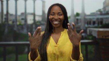 Şehir ortamında gülümseyen, sarı giyinen neşeli havayı vurgulayan, doğal gün ışığı altında manzaraya karşı kendine özgü örgüleri olan bir kadın..