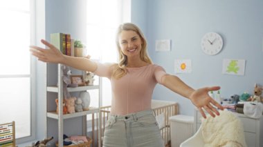 Sıcak bir yatak odasında gülümseyen kadın oyuncaklar, kitaplar ve çocuk odası dekorlarıyla çevrili, doğal ışıkla aydınlatılmış, sıcak ve davetkar bir atmosfer yaratıyor..