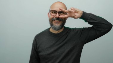 Sakallı kel bir adam, parmaklarıyla izole edilmiş beyaz bir arkaplan üzerinde barış işareti yapıyor..