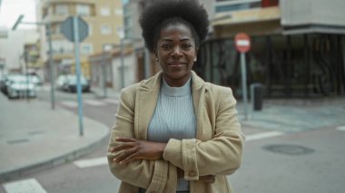 Şehir sokaklarında gülümseyen bir kadın kolları çaprazlanmış bir ceket giyiyor kentsel bir çevrede binalar ve arabalarla çevrili..