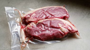 Açık gri bir yüzey üzerinde taze kırmızı biftekli vakumlanmış paketler depolanmaya ya da pişirmeye hazır çiğ mermer et sergiliyorlar.