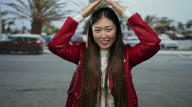 Kırmızı ceketli kadın arka planda bulanık arabalarla şehir caddesinde neşe içinde poz veriyor..