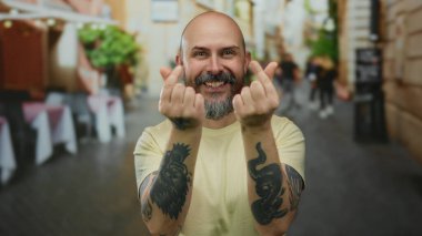 Dövmeli kel bir adam şehir sokaklarında kalp hareketi yapıyor neşeli bir havayı somutlaştırıyor ve canlı bir şehir ortamında rahat bir ortam yaratıyor..