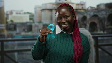 Elinde mavi kurdele tutan kadın antik Roma harabelerinin yanında gülümsüyor, şehir ortamındaki modernlikle mirası harmanlıyor..