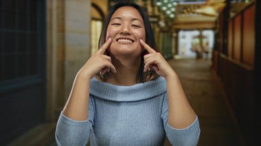 Canlı bir şehir caddesinde gülümseyen genç bir kadın dükkanların ve ışıkların bulanık arka planıyla.